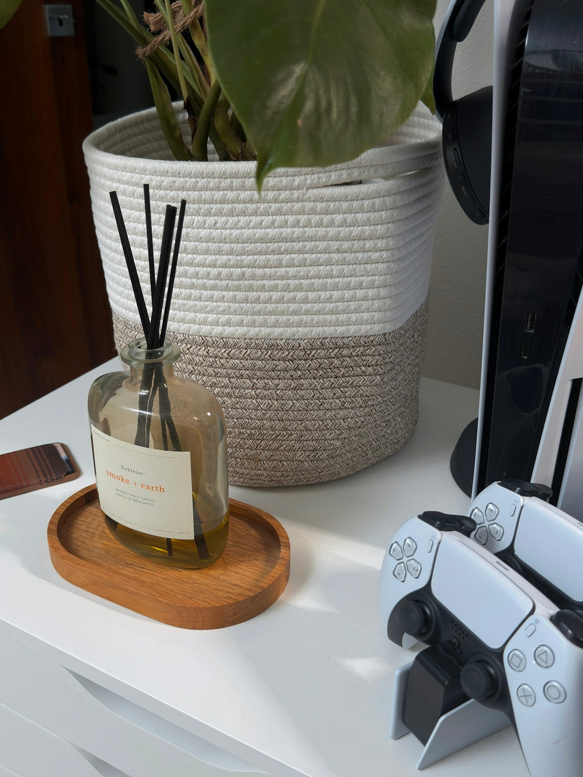 Reed diffuser on wooden tray next to game controllers.